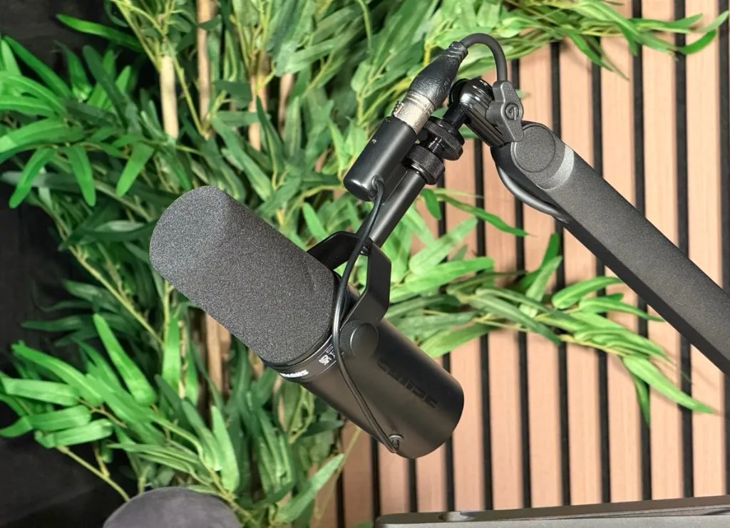 Shure SM7dB microphone on a boom arm in front of green plants and wooden acoustic panelling